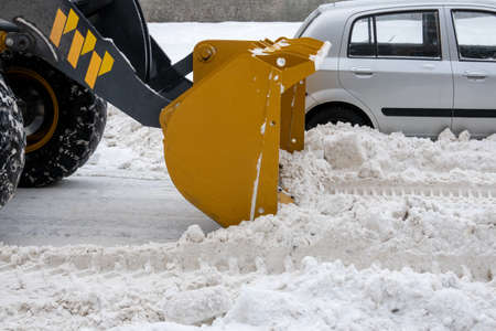 A tractor with a bucket rakes snow from the roadway. Selective focus.