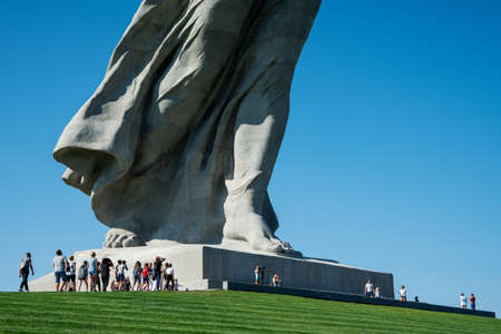 Russia, Volgograd, August 25, 2020: a group of people near a giant sculpture of a woman. The image of the sculpture is cut off, showing the legs and lower part of the dress.のeditorial素材