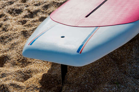 A cut-off image of a swimming Board with a fin embedded in the sand. Copy space.