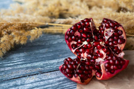 A broken ripe pomegranate on a blue wooden table. Food paper is placed under the pomegranate, and pampas grass is lying next to it. Copy space. Selective focus.の写真素材