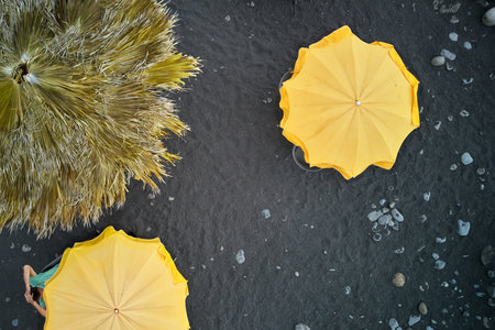 Yellow umbrellas against the background of black volcanic sand. A man is lying under one of the umbrellas. Shooting from a drone.の写真素材