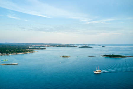 The winding picturesque coast of Croatia with small islands near the coastline. A tourist boat is...