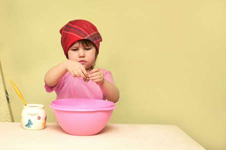 A little girl kneads the dough. She breaks an egg into a pink dish. Copy space.
