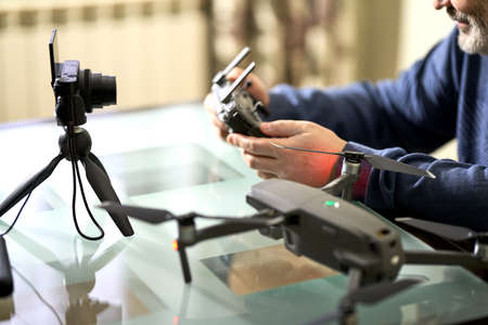 A man writes a blog in front of a camera about taking photos with a quadrocopter. He is holding the...