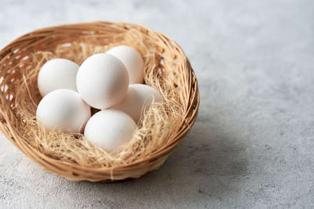 White chicken eggs in a wicker basket on a gray background. Selective focus. Copy space.の写真素材