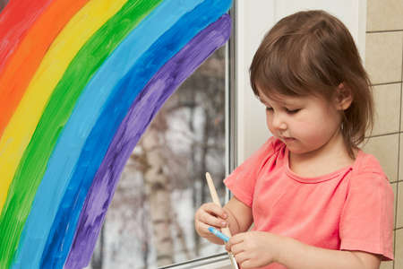 Portrait of a little girl of a rainbow painted on the window.の写真素材