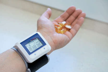 A man's hand with a blood pressure monitor on his wrist and a medicine in the palm of his hand. Selective focus.の写真素材