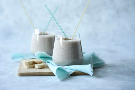 Two glasses with a milky banana cocktail on a bluish gray background. There are two straws in each glass. Next to the glasses are banana circles. Copy space. Selective focus.の写真素材