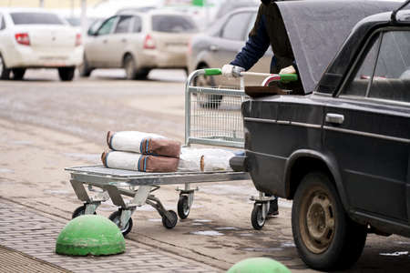 Parking near the construction shop. The man loads the purchased construction materials into the trunk of the car. Selective focus.の写真素材