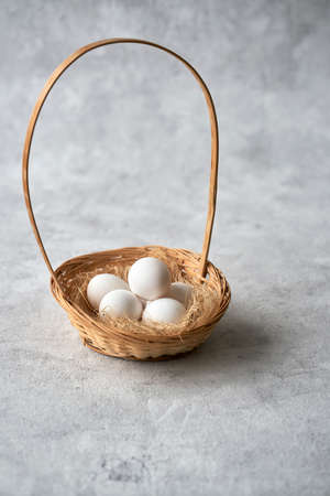 Wicker basket with white chicken eggs on a gray textured background. Selective focus. Copy space.
