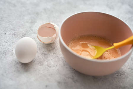 A bowl with egg mass on a gray textured background. Next to it is an egg and the shell of an egg. Selective focus. Copy space.の写真素材