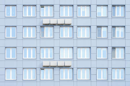 The facade of a residential building, lined with aluminum panels. Air conditioners hang on the...