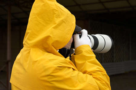 Photography in bad weather. A man in a yellow raincoat takes photos with a camera with a telephoto...