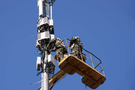 Installation of cellular equipment on the tower. Two communications engineers work at altitude from...