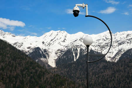A lantern and a rotary video surveillance camera on one support against the background of mountains...