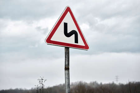 Triangular road sign dangerous turn on the background of a rainy sky. Selective focus. Copy space.