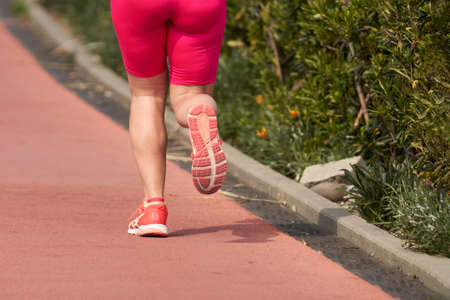 A cut-off image of a running woman in pink sports shorts: legs, thighs, buttocks. Selective focus.