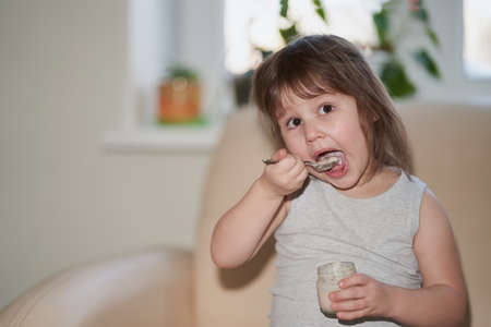 The baby with an appetite eats baby puree from a jar. She lifted the food spoon to her open mouth. Selective focus.の写真素材