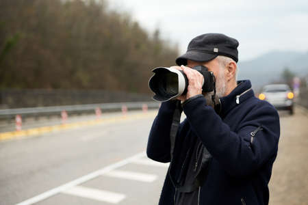 An adult man takes photos with a long-focus lens on a mountain road. Selective focus. Copy space.