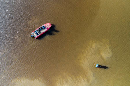Men's company on a fishing trip. Two are fishing on a spinning boat, one is standing knee-deep in the water. Shooting from a drone.の写真素材