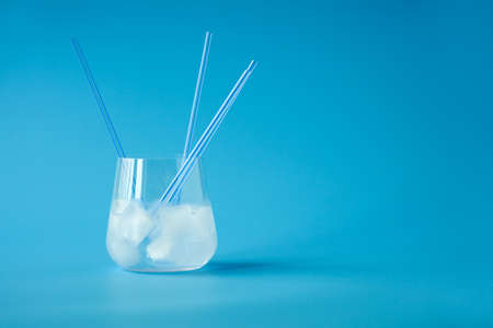 A glass with a clear drink, ice cubes and a few straws on a pale blue background. Copy space.の写真素材