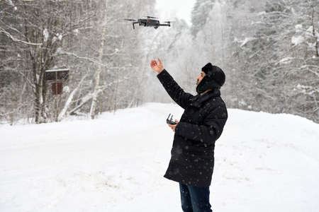 Shooting from a drone in winter in a snowfall. A man with a drone on the road in the forest. The...