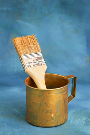 An old tin mug with a paint brush on a blue background. Selective focus.の写真素材