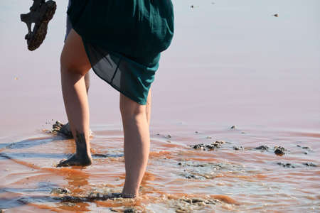 A man and a woman barefoot cross the flooded area after a downpour. The man holds the removed shoes in his hands. A woman supports the hem of her dress with her hand.の写真素材