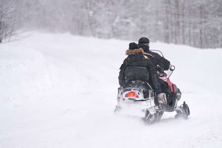 Two men are racing on a snowmobile through snowdrifts in the forest. Snow is falling. Selective...