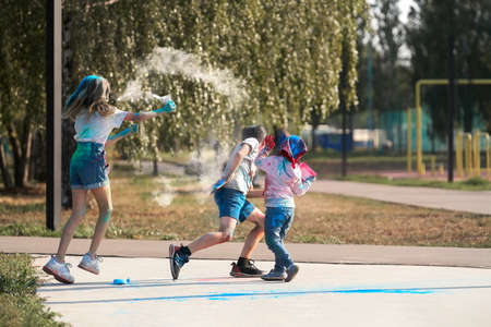 Children's holiday with holi colors. A girl sprays powder, a boy and a baby dodge a cloud of dust.