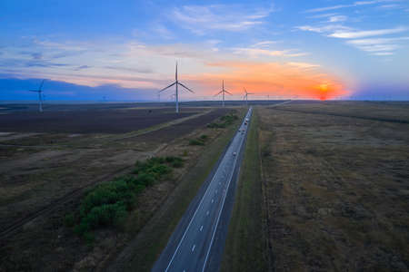 Three-bladed wind generators along the highway at sunset. Shooting from a drone.の写真素材