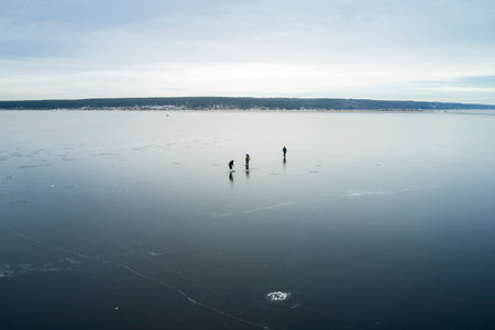 Ice fishing. Three fishermen on the thin ice of a frozen pond. Shooting from a drone.