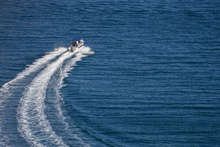 A lone motorboat is moving at speed on the blue sea surface. A white wake stretches behind her. Copy...