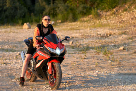 A girl on a red motorcycle in nature in the soft light of the setting sun. Selective focus. Copy...