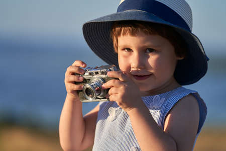 Portrait of a little girl in a straw hat with an analog camera in her hands. Vintage. Copy space.の写真素材
