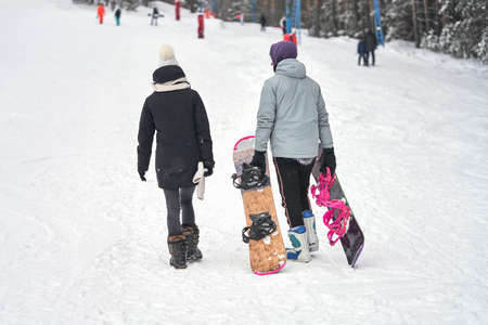 Ski resort. A guy and a girl climb a snowy mountainside. The guy carries two boards. A t-bar lift passes to their right. Selective focus.の写真素材