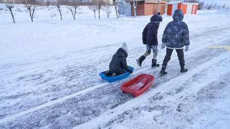 The boys are returning from a winter walk. They are walking along the road, pulling a sled behind...