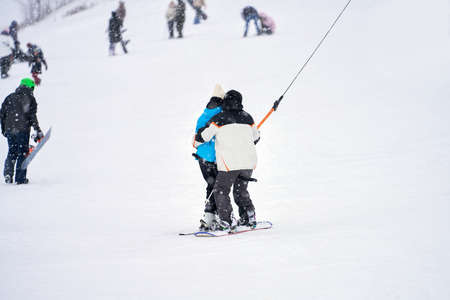 The rise of snowboarders on the slope in pairs on the T-bar lift. Snowfall. Selective focus.