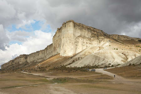 Rocky canyon on a cloudy day. At the foot of the cliff is a playground with parked cars.