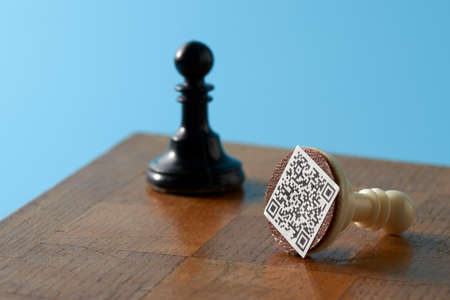 Black and white pawns on an old chessboard. The white pawn has a QR code based on it. The background...
