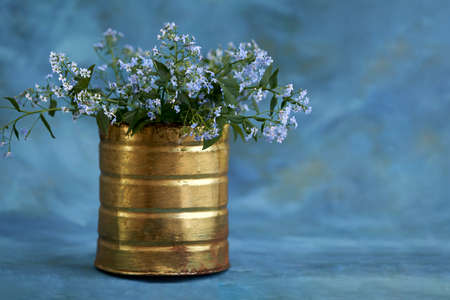 Exquisite simplicity of a bouquet of wildflowers. An old gilded jar with forget-me-nots on a blue background with light gilding. copyspace.の写真素材