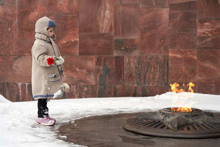 memorial complex. A little girl stands in front of the eternal flame with a carnation flower in her hand. copyspace.の写真素材