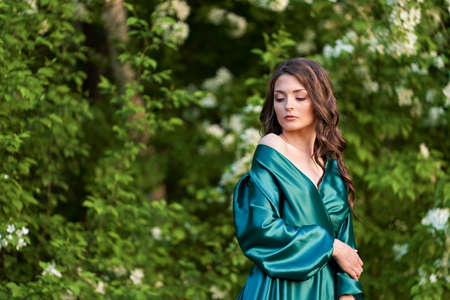 Portrait of a green-eyed beauty in green silk clothes against a background of blooming apple trees. copyspace.の写真素材