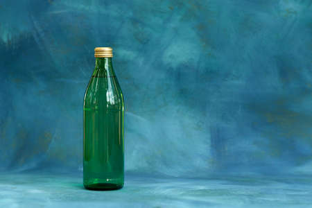 A bottle of green glass with a drink on a blue background with light gilding. copyspace.の写真素材