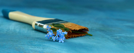 A painting flat brush with a branch of forget-me-nots in the bristles on a blue background....