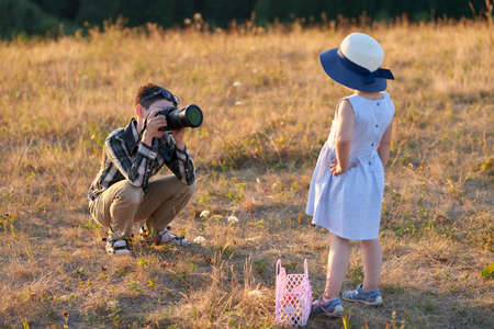 A teenage boy takes pictures of his younger sister with a camera in nature in the soft light of the setting sun. copyspace. selective focus.の写真素材