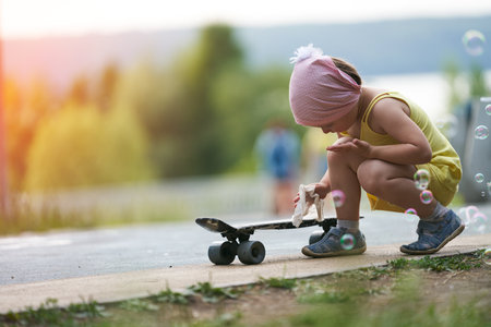 A little girl in the setting sun wipes a skateboard with a wet cloth after riding in the park. selective focus.の写真素材