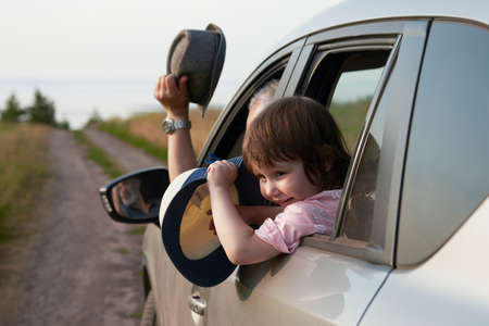 A fragment of a car with a happy child in the window. A motorist and a girl wave straw hats as they approach the seashore. selective focus.の写真素材