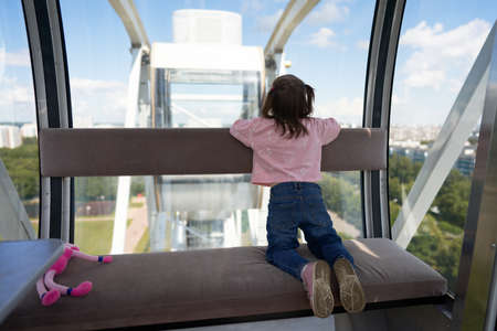 Ferris wheel. The cabin for passengers from the inside. The girl looks out the window at the panorama of the city from a height.の写真素材