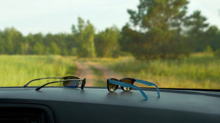 Protection of the motorist's vision from the sun. Sunglasses on the dashboard of the car. Through the windshield there is a beautiful view of the field and the forest.の写真素材